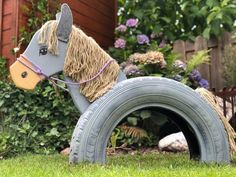 a toy horse is sitting on top of a tire in the grass with flowers behind it