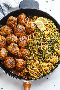 spaghetti and meatballs in a skillet with lemon wedges on the side, ready to be eaten