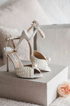 a pair of white high heeled shoes sitting on top of a box next to a flower