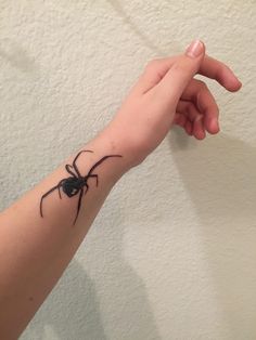 a person's arm with a black spider tattoo on it, and one hand holding the other