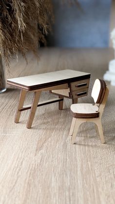 a miniature desk and chair sitting on the floor in front of a vase with dry grass