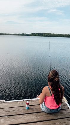 a woman sitting on a dock with a fishing pole in her hand and a can of water next to her