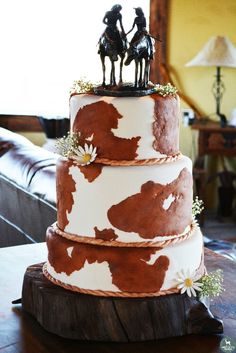 a three tiered cake decorated with brown and white cow print icing, topped with two figurines