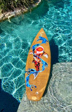 an orange surfboard sitting on top of a rock next to a pool filled with blue water