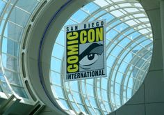 a comic convention sign hanging from the side of a glass dome in an indoor building