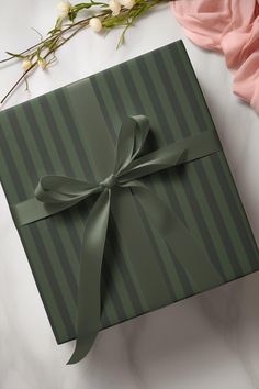 a green gift box with a bow on it and flowers in the corner next to it