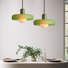 two green lights hanging over a table with plates and bowls on it in front of a window