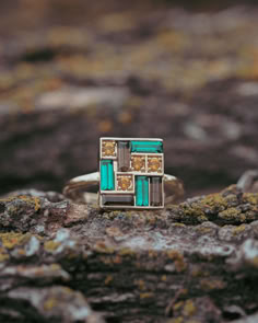 A unique engagement ring from Staghead Designs sits on a lichen-covered log. This 14K yellow gold ring features a rectangular head with four round citrine accents, three baguette smoky quartz accents, and three baguette cut lab-grown emerald accents arranged in a mosaic. This ring almost looks like a piece of stained glass. Gem Engagement Ring, Whiskey Barrel Wedding Ring, Antler Wedding Ring, Multi Gem Ring, Wedding Bands Rose Gold, Antler Wedding Rings, Whiskey Barrel Wedding, Gem Engagement Rings, Meaningful Rings