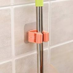 a shower head with an orange and green handle on the wall next to a white tiled wall