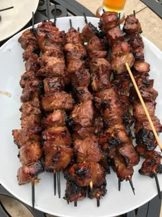 a plate with skewers of meat on it and a glass of beer in the background