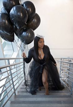 a woman in a black dress is walking down the stairs with balloons on her head