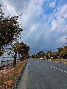 an empty street lined with palm trees under a cloudy sky