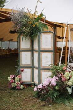 A rustic wedding seating chart display featuring a folding screen adorned with floral arrangements and seating cards. Framed Table Seating Chart, Summer Seating Chart, Micro Wedding Seating Chart, Winery Wedding Seating Chart, Seating Arrangement Wedding Display, Classic Seating Chart, Picture Frame Seating Chart Wedding, Unique Seating Chart Wedding Display, Interactive Wedding Seating Chart