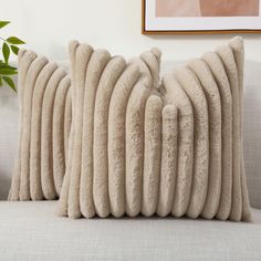 two beige pillows sitting on top of a couch next to a potted green plant