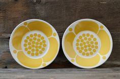 two yellow and white plates sitting on top of a wooden table next to each other