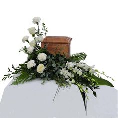 white flowers and greenery sit on top of a wooden box in the shape of a casket