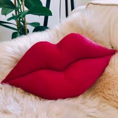 a white fur covered couch with a red pillow on it's side and a plant in the background