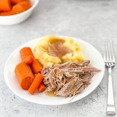 a white plate topped with meat, mashed potatoes and carrots next to a fork