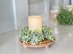 a lit candle sitting on top of a wooden stand with greenery in the background