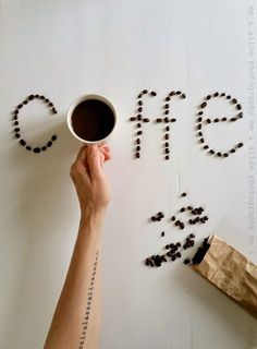 a person holding a coffee cup in front of the word coffee spelled out with coffee beans