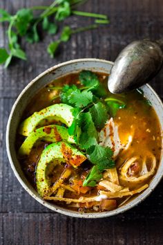 an overhead view of a bowl of soup with avocado and cilantro