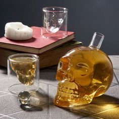 two glasses and a skull shaped bottle on a table next to a book with a candle in it