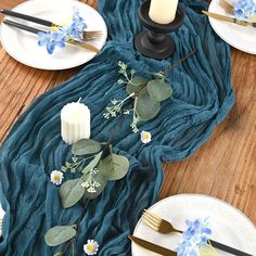 the table is set with plates, silverware and blue flowers on top of it