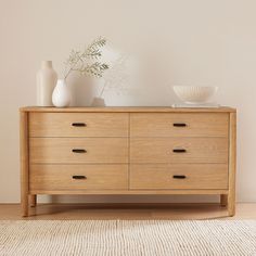 a wooden dresser sitting on top of a rug next to a white vase and bowl