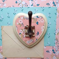 an envelope with a heart shaped handle attached to it, sitting in front of a floral wallpaper