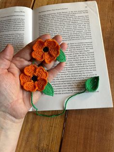 a hand holding two crocheted flowers on top of an open book