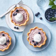 three blueberry pies with whipped cream on top and fresh berries around the edges