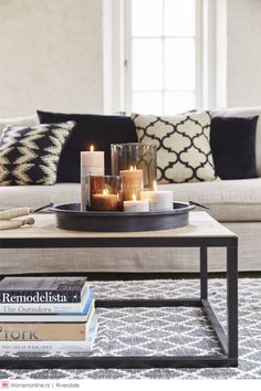 candles are lit on a tray in front of a coffee table with books and pillows