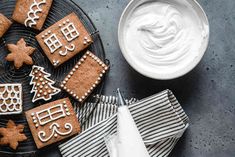 gingerbreads with icing and decorated cookies on a plate next to a bowl of whipped cream