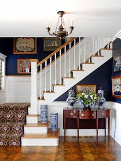 a staircase with blue and white vases on the table next to it, along with pictures on the wall