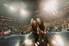 two men standing on top of a stage in front of an audience at a concert