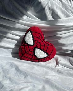 a crocheted spiderman heart sitting on top of a white sheet with eyes