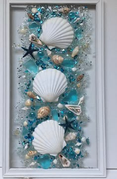 sea glass and seashells are displayed in a white frame on the side of a wall