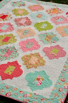 a large quilt is laying on the ground in front of some green grass and flowers