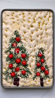 a cake decorated with christmas trees and cherries on white frosting in a pan