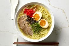 a bowl of ramen with meat, eggs and vegetables on top next to chopsticks