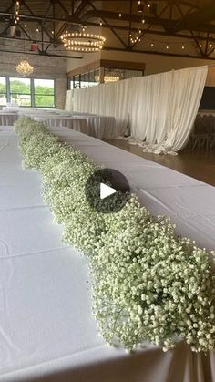 a long table with flowers on it in front of a window and white drapes