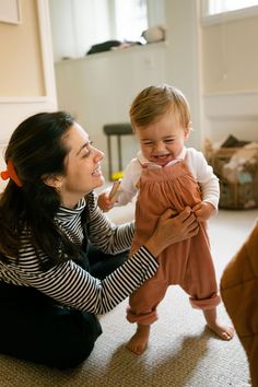 a woman is holding a baby in her arms and smiling at the camera while sitting on the floor