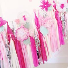 pink and white streamers hanging from the ceiling with flowers on them at a birthday party