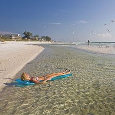 a woman laying on top of a blue surfboard in the ocean next to a sandy beach