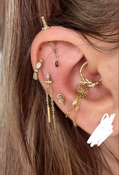 a woman wearing gold ear piercings with chains and charms on her ears, in front of