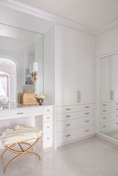 a white dressing room with large mirror and gold handles on the dresser, along with an ottoman