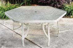 a white table sitting on top of a cement ground next to some bushes and flowers