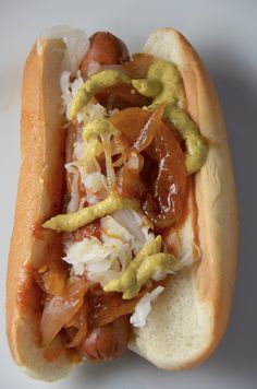 a hot dog with mustard, onions and ketchup on a white bun covered in condiments