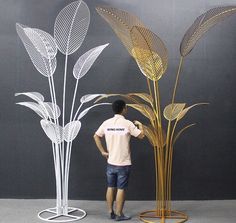 a man standing in front of two tall metal plant sculptures, one with leaves on it