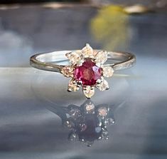 Item: Vintage 18K White Gold Ruby Red Spinel Diamond Halo Cluster Ring. This is stamped and tested 18K gold. The red stone is testing as Spinel. The white stones are testing as diamonds using a Presidium Gemstone tester. The ring box is not included in the sale of the ring. Measurements: Size 5.5. It weighs 2.03 grams. The spinel measures 4mm across. The diamonds each measures approximately 1.75mm. Condition: Vintage, previously owned. Visible under magnification are some light scratches/wear on the red stone. Please see our other listings, we combine shipping for savings. Red Spinel, Spinel Ring, White Stones, Red Stone, Diamond Halo, Cluster Ring, Ring Box, Ruby Red, Halo Diamond